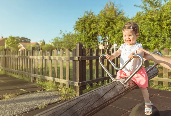 Baby girl playing over a seesaw swing on the park — Stock Photo, Image