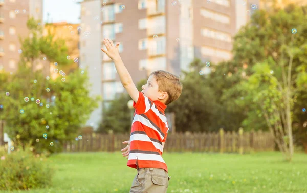 Щасливий хлопчик грає з мильними бульбашками в парку — стокове фото