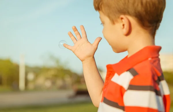 Rapaz bonito olhando bolha de sabão em sua mão aberta — Fotografia de Stock