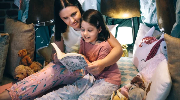Chica leyendo con su madre en una tienda improvisada — Foto de Stock