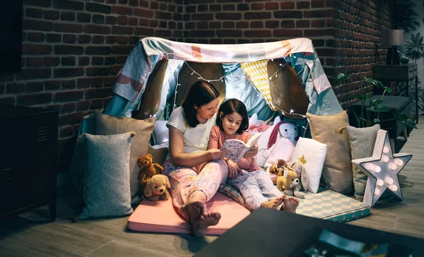 Anne ve kızı pijama partisi verip kitap okuyorlar. — Stok fotoğraf