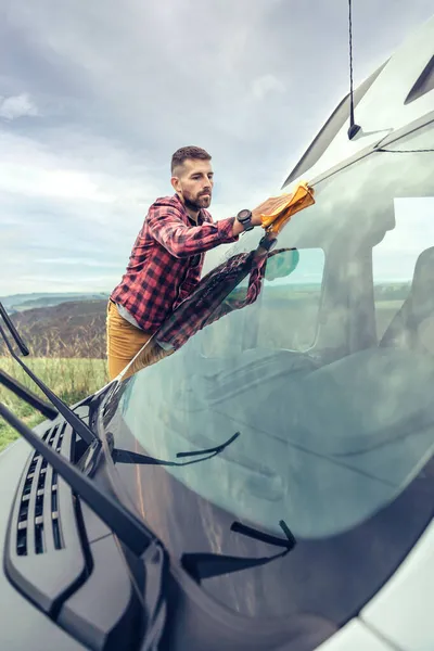 Man cleaning camper van windshield outdoor