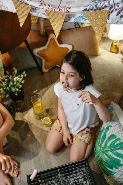 어린 소녀 가집에서 캠핑을 하고 볶은 마시멜로를 먹고 있다 — 스톡 사진