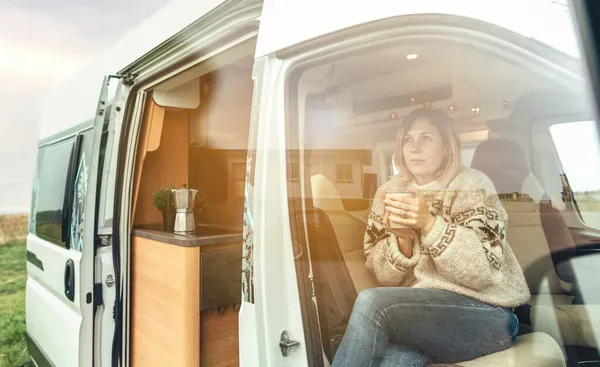 Mulher com um copo sentado no banco da frente de uma van campista — Fotografia de Stock