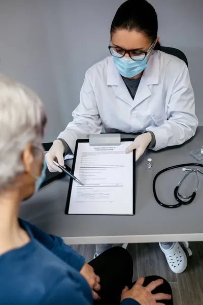 Ärztin erklärt ihrem Patienten Einverständniserklärung zum Coronavirus-Impfstoff — Stockfoto