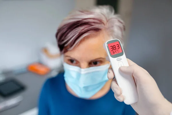 Wanita senior dengan demam yang suhunya diambil oleh dokternya — Stok Foto