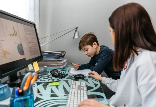 Mother helping her son with his homework while teleworking — Stock Photo, Image