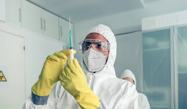 Médico con traje protector que mira y prepara la jeringa con la vacuna — Foto de Stock