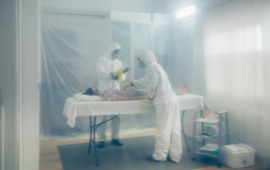 Bakteriyolojik koruma altındaki doktorlar sedyede yatan hastaya tıbbi muayene yapıyorlar.