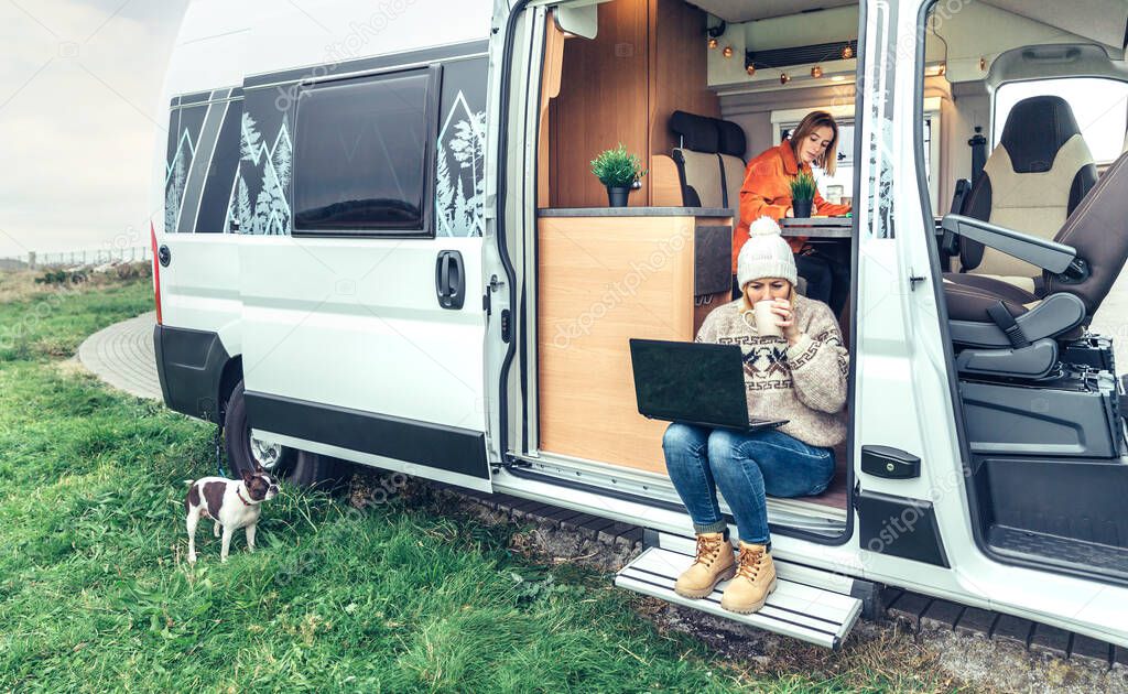 Woman teleworking drinking coffee sitting in the door of a camper van