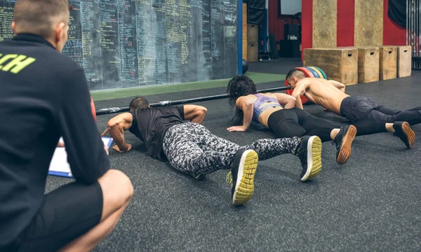 Az emberek a tornateremben fekvőtámaszoznak, miközben az edzőjük figyeli őket. — Stock Fotó