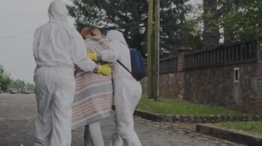Doctors in protection suits walking with sick woman outdoors