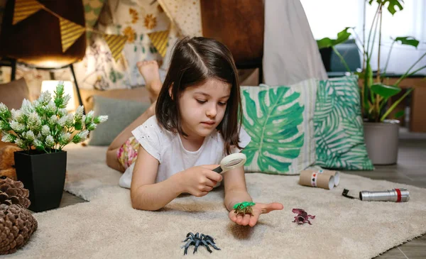 Menina jogando observando insetos de brinquedo com uma lupa — Fotografia de Stock