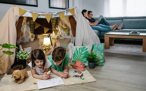 Kinder zelten zu Hause, während ihre Eltern lesen und aufs Handy schauen — Stockfoto