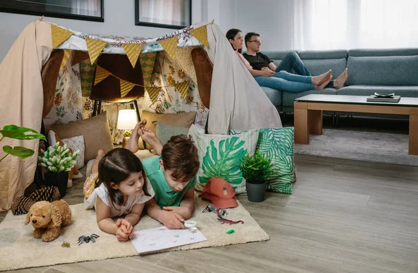 Niños jugando a acampar en casa mientras sus padres ven la televisión —  Fotos de Stock