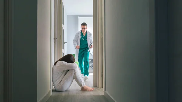 Bezorgde dokter loopt om geestelijke stoornis patiënt zitten op de vloer in het ziekenhuis gang te helpen — Stockfoto