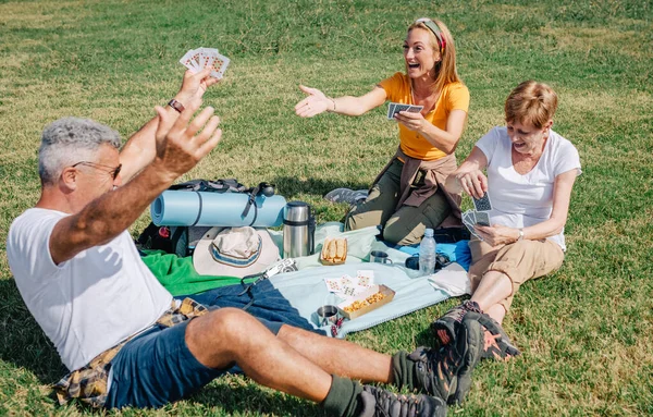 Uomo anziano che festeggia di aver vinto la sua famiglia giocando a carte durante un'escursione — Foto Stock