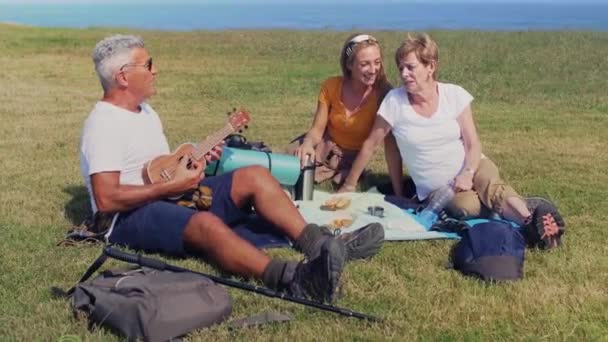 Família adulta tocando ukulele e cantando sentado em um cobertor durante uma excursão — Vídeo de Stock