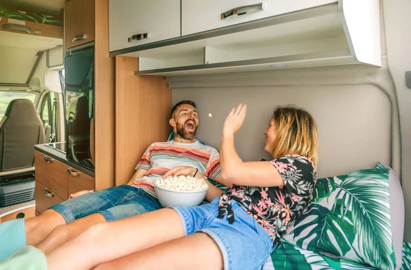 Woman throwing a popcorn into her boyfriends mouth lying on the bed of their camper van — ストック写真