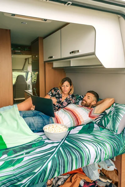 Casal deitado assistindo a um filme com roupas bagunçadas e sapatos sob a cama de sua campervan — Fotografia de Stock