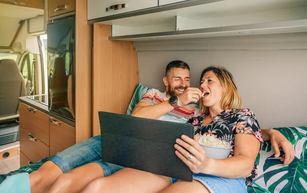 Homem alimentando sua namorada uma pipoca assistindo um filme no tablet em sua van campista — Fotografia de Stock