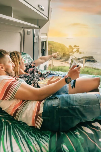 Coppia guardando un film sul tablet mangiare popcorn sdraiato sul letto del loro camper — Foto Stock