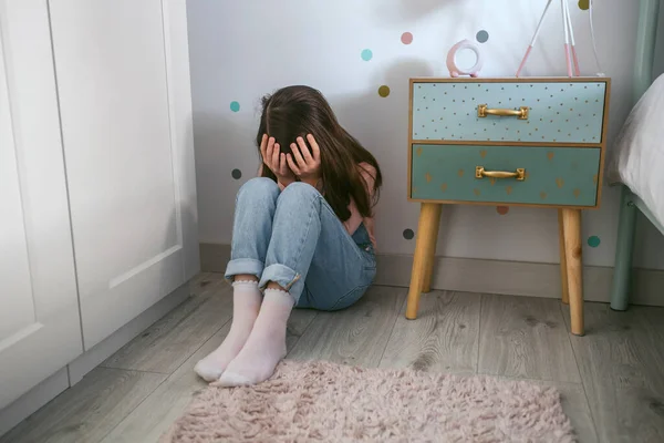 Неузнаваемая маленькая девочка, закрывающая лицо руками, сидящими на полу — стоковое фото