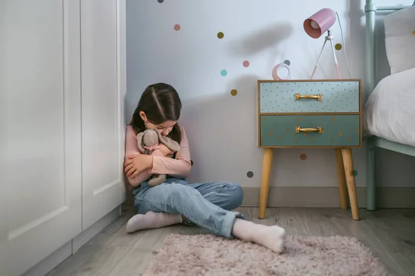 Gadis sedih memeluk boneka mainan duduk di lantai — Stok Foto