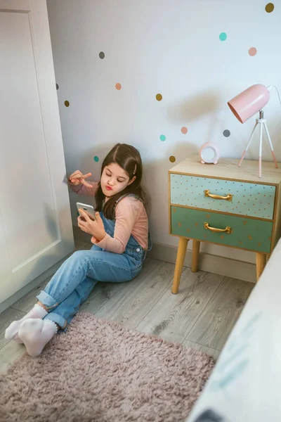 Girl with duck face taking selfie with cell phone for social media sitting on the floor — Stock Photo, Image