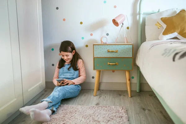 Chica riendo mirando el móvil sentado en el suelo — Foto de Stock