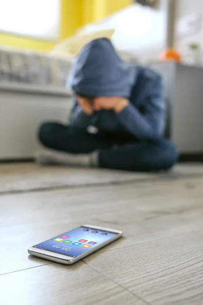 Tiener jongen huilen wanhopig voor pesten met mobiele telefoon liggend op de vloer in de voorgrond — Stockfoto