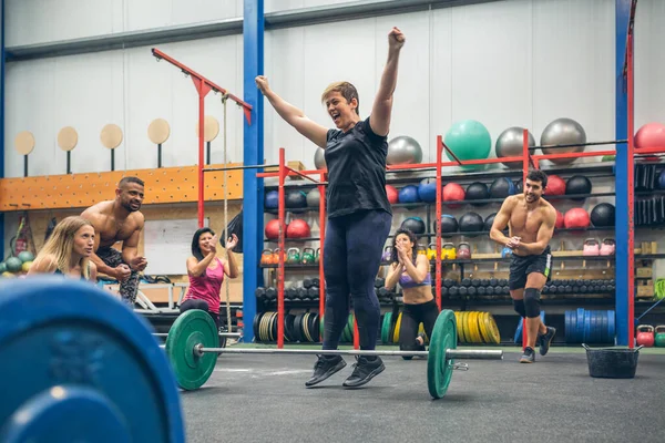 Mujer feliz celebrando su logro de levantamiento de pesas mientras sus compañeros de gimnasio la animan —  Fotos de Stock