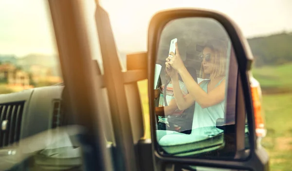 Reflectie in een camper achteruitkijkspiegel van een vrouw die een foto neemt met haar mobiele telefoon — Stockfoto