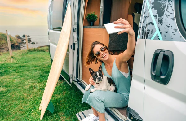 Young woman taking photo sitting with her boston terrier dog at the door of camper van
