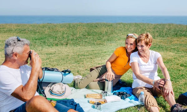 お父さんがカメラを持って幸せな家族に写真を撮るピクニックを屋外で持っている毛布の上に座って — ストック写真