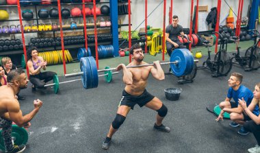 Strong man practicing weightlifting in the gymnasium with his partners cheering him on
