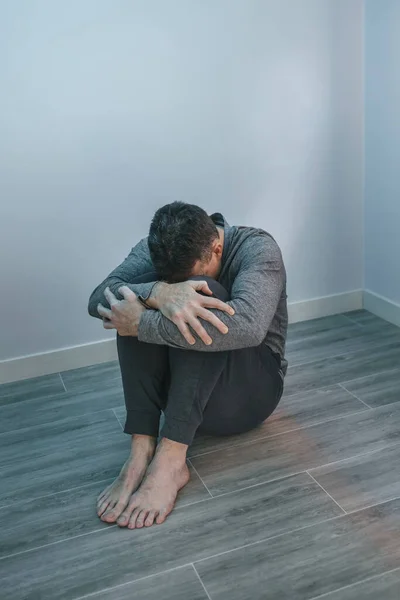 Unrecognizable desperate man with problems resting his head on arms sitting on the floor
