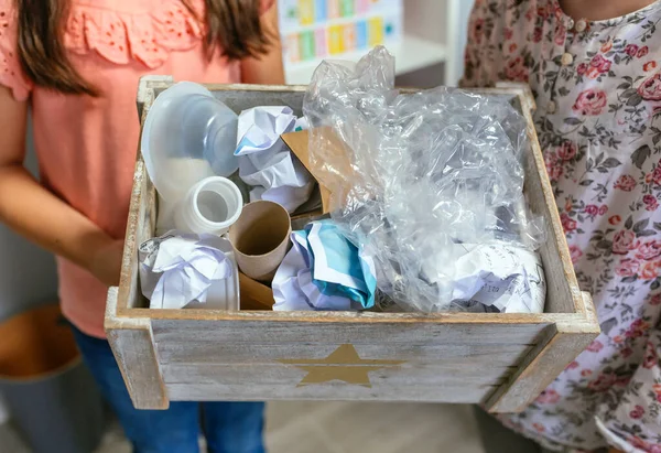 生態学教室の2人の無名の女の子がリサイクルする廃棄物の箱を示しています — ストック写真