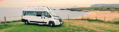 Yaz günbatımında boş plajın yanına park edilmiş panoramik karavan manzarası.