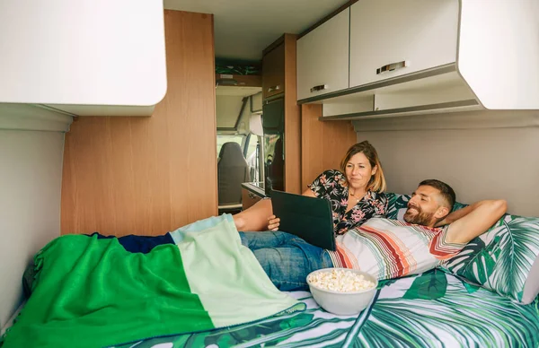 一对笑着的年轻夫妇躺在他们野营车的床上看平板电脑上的一部电影 — 图库照片