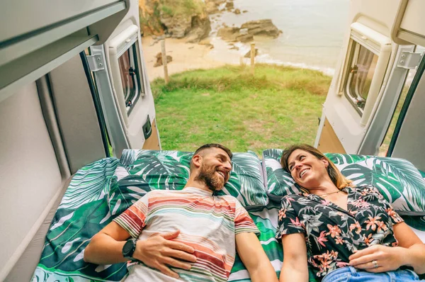 幸せなカップルお互いを見て彼らのキャンパーバンのベッドの上に横たわって ドアが海岸の風景に向かって開いている — ストック写真