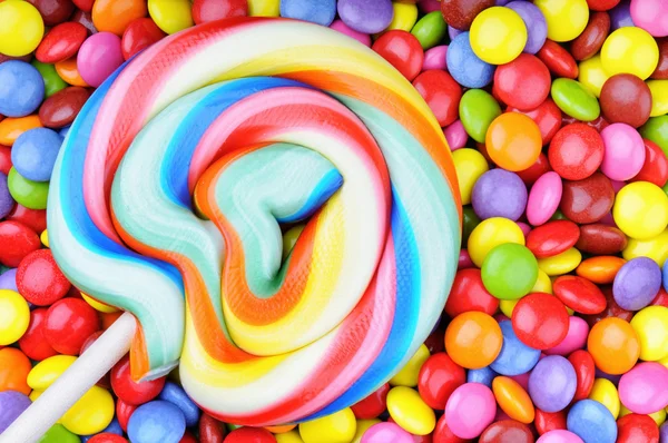 Striped lollipop and multicolored smarties — Stock Photo, Image