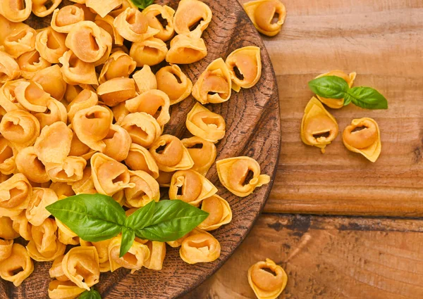 Tortellini na dřevěné desce s bazalkou a parmezánem. Specialities of the cuisine from Bologna and Emilia Romagna: Cappelletti, fresh egg pasta with meat and vegetables filling. — Stock fotografie