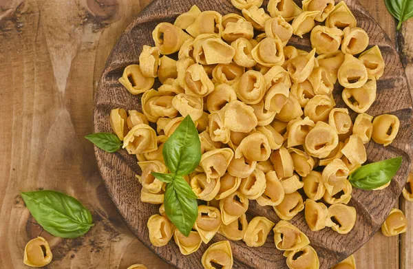 Tortellini na dřevěné desce s bazalkou a parmezánem. Specialities of the cuisine from Bologna and Emilia Romagna: Cappelletti, fresh egg pasta with meat and vegetables filling. — Stock fotografie