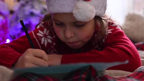 Doce criança está escrevendo uma carta para Papai Noel no quarto, decorado para o Natal, preparando-se para férias espírito de Natal, feriados e celebrações conceito — Vídeo de Stock
