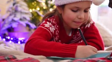 Tatlı çocuk Noel Baba 'ya bir mektup yazıyor, Noel için süslenmiş, Noel ruhuna, bayramlara ve kutlamalara hazırlanıyor.