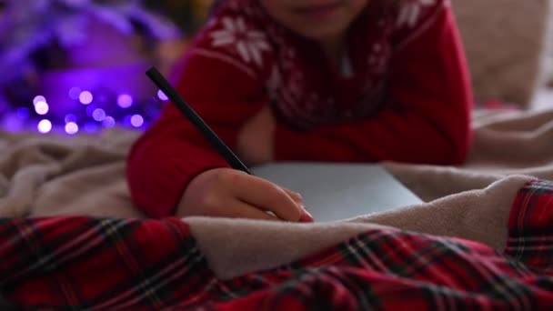 Doce criança está escrevendo uma carta para Papai Noel no quarto, decorado para o Natal, preparando-se para férias espírito de Natal, feriados e celebrações conceito — Vídeo de Stock