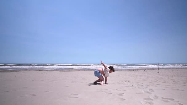 Genç jimnastikçi kadın jimnastik öğeleri kumsalda gerçekleştirme. — Stok video