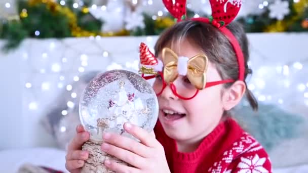 Портрет новорічної дівчини. Маленька дівчинка відкриває сюрприз з різдвяним м'ячем. Емоції щастя і задоволення . — стокове відео