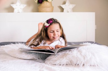 Öğrenci kız odada kitap okuyordu. 8 ya da 10 yaşında bir kız. Yatağın üstündeki odada bir kitap var. Evde okumak için parlak bir iç mekanda bir çocuk.